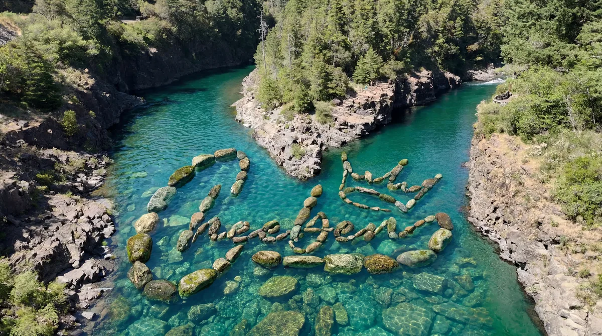 AI visualization of the Cheeben logo arranged in river stones in an emerald Southern Oregon river