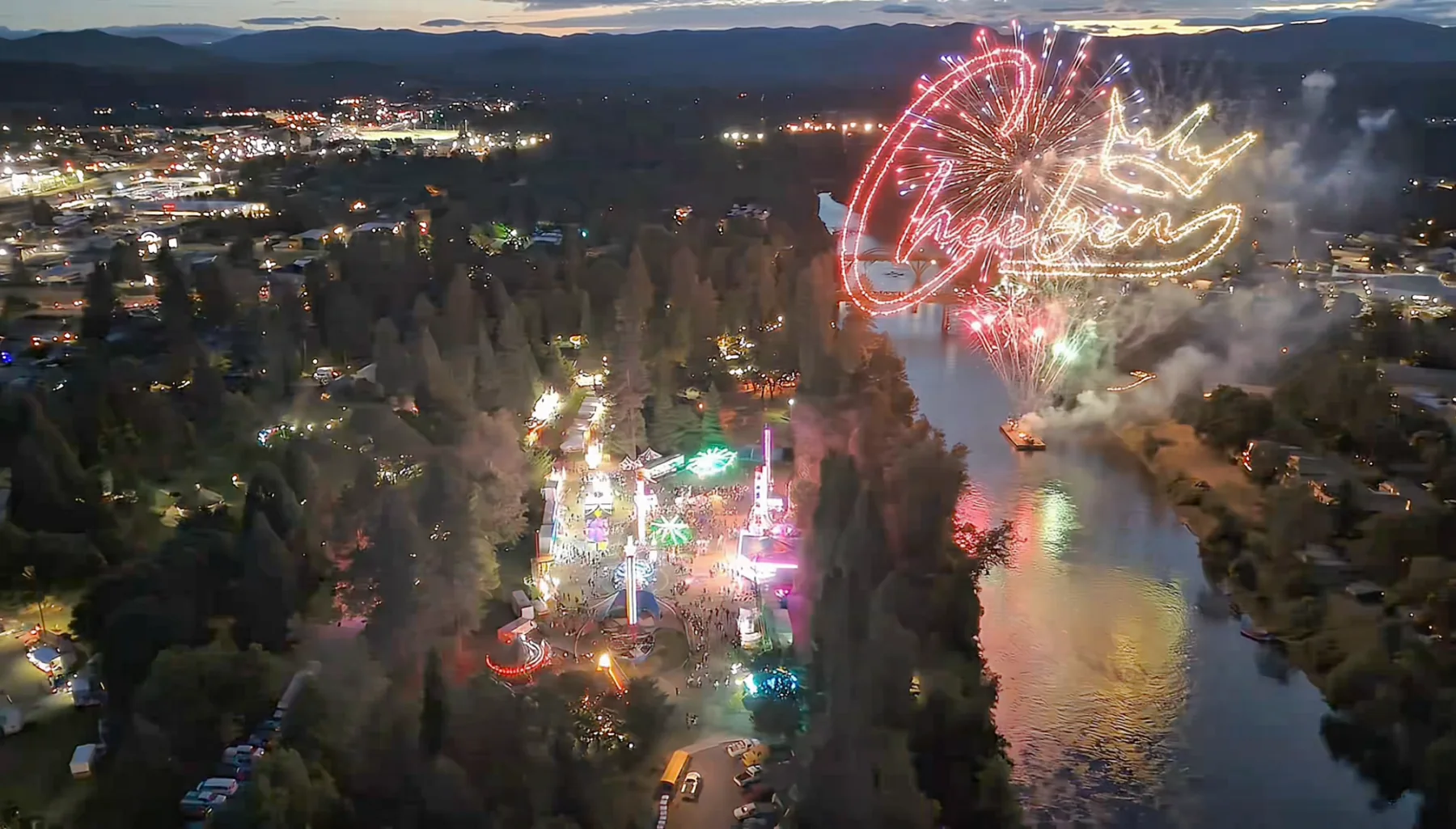 Aerial evening view of Grants Pass with fireworks and a luminous Cheeben logo
