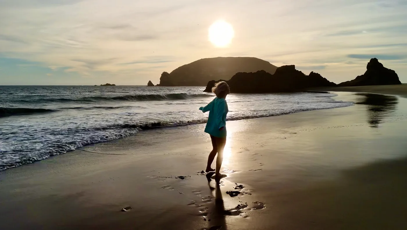 Drone photograph of a woman walking at sunset on the Southern Oregon coast near sea stacks